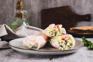 Spring rolls in rice paper with crab sticks, cucumber, greens and sauce on a plate on the table photo