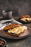 Sweet sandwich with chocolate butter, banana and nuts on a plate on the table vertical view photo