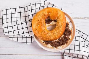 Close up of bagel sandwich with butter and grated chocolate on a plate on a table top view photo