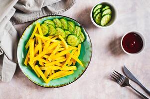 Appetizing French fries and cucumber slices on a plate on the table top view photo