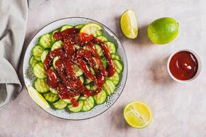 Mexican spicy cucumbers with chili sauce and lime on a plate on the table top view photo