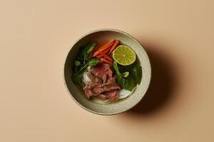 Top-down view of a steaming bowl of traditional Vietnamese pho with beef, rice noodles, fresh herbs, lime, and vegetables. photo