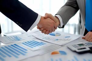 Business professionals engage in a handshake during a meeting to finalize a contract near financial reports and charts photo