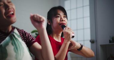 Two Asian women sitting on a sofa happily singing karaoke with smiles and enjoying a fun time together at home. Share good times, Enjoy a warm moment video