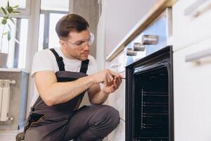 Professional plumber repairing oven using screwdriver in kitchen photo