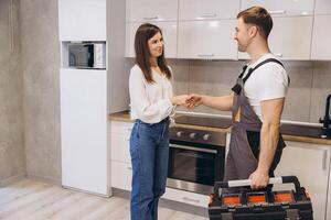 Plumber shaking hands with woman in kitchen after finishing work photo