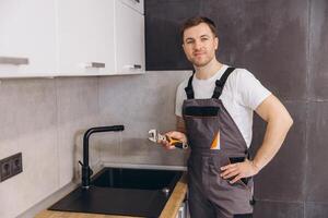 Plumber holding an adjustable wrench and working on a kitchen faucet photo