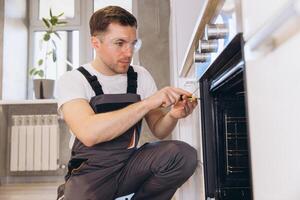 Professional plumber repairing oven in kitchen using screwdriver photo