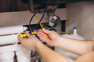 Plumber tightening a screw under the kitchen sink using a screwdriver photo