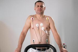 A middle-aged man is undergoing a medical stress test on a treadmill, connected to ECG electrodes for heart monitoring in a clinical environment photo
