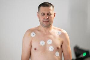 A middle-aged man is undergoing a medical stress test on a treadmill, connected to ECG electrodes for heart monitoring in a clinical environment photo