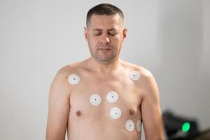 A middle-aged man is undergoing a medical stress test on a treadmill, connected to ECG electrodes for heart monitoring in a clinical environment photo
