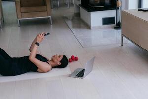 A sportswoman using a smartphone while resting and lying on the modern house floor photo