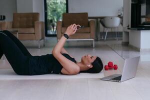 A sportswoman using a smartphone while resting and lying on the modern house floor photo