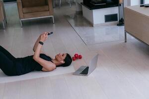 A sportswoman using a smartphone while resting and lying on the modern house floor photo