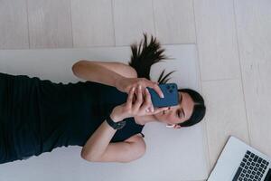 Sportswoman using a smartphone while resting and lying on the floor of modern house. photo