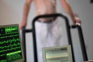A middle-aged man is undergoing a medical stress test on a treadmill, connected to ECG electrodes for heart monitoring in a clinical environment photo