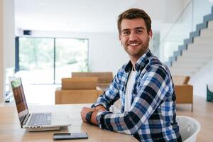 A freelancer sitting at a table in a modern living room, with headphones using a laptop for business chat, conversation with friends and entertainment photo