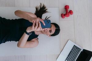 Sportswoman using a smartphone while resting and lying on the floor of modern house. photo