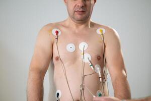 A middle-aged man is undergoing a medical stress test on a treadmill, connected to ECG electrodes for heart monitoring in a clinical environment photo