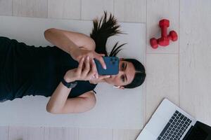 Sportswoman using a smartphone while resting and lying on the floor of modern house. photo