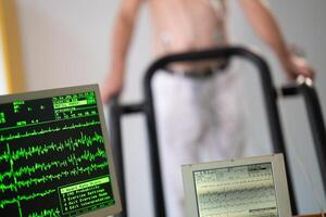 A middle-aged man is undergoing a medical stress test on a treadmill, connected to ECG electrodes for heart monitoring in a clinical environment photo