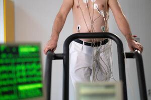 A middle-aged man is undergoing a medical stress test on a treadmill, connected to ECG electrodes for heart monitoring in a clinical environment photo