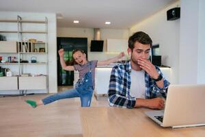 Work from home. Daughter interrupting her father while he is having a business online conversation on his laptop while sitting in the modern living room. photo