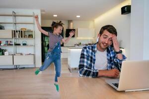 Work from home. Daughter interrupting her father while he is having a business online conversation on his laptop while sitting in the modern living room. photo