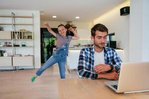 Work from home. Daughter interrupting her father while he is having a business online conversation on his laptop while sitting in the modern living room. photo