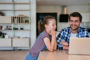 Work from home. Daughter interrupting her father while he is having a business online conversation on his laptop while sitting in the modern living room. photo