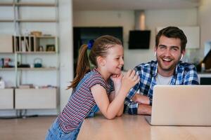 Work from home. Daughter interrupting her father while he is having a business online conversation on his laptop while sitting in the modern living room. photo