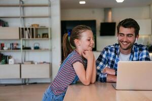Work from home. Daughter interrupting her father while he is having a business online conversation on his laptop while sitting in the modern living room. photo