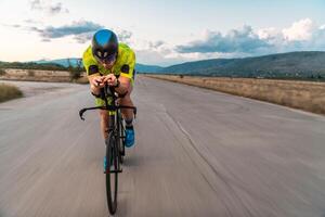 Triathlete riding his bicycle during sunset, preparing for a marathon. The warm colors of the sky provide a beautiful backdrop for his determined and focused effort. photo