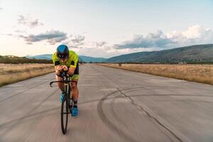 Triathlete riding his bicycle during sunset, preparing for a marathon. The warm colors of the sky provide a beautiful backdrop for his determined and focused effort. photo