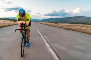 Triathlete riding his bicycle during sunset, preparing for a marathon. The warm colors of the sky provide a beautiful backdrop for his determined and focused effort. photo