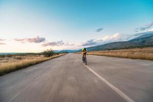 Triathlete riding his bicycle during sunset, preparing for a marathon. The warm colors of the sky provide a beautiful backdrop for his determined and focused effort. photo