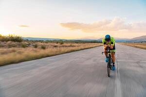 Triathlete riding his bicycle during sunset, preparing for a marathon. The warm colors of the sky provide a beautiful backdrop for his determined and focused effort. photo