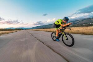 Triathlete riding his bicycle during sunset, preparing for a marathon. The warm colors of the sky provide a beautiful backdrop for his determined and focused effort. photo
