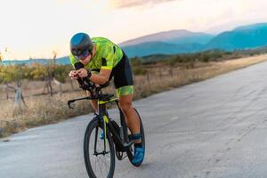 Triathlete riding his bicycle during sunset, preparing for a marathon. The warm colors of the sky provide a beautiful backdrop for his determined and focused effort. photo