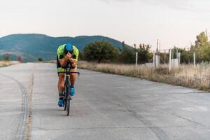 Triathlete riding his bicycle during sunset, preparing for a marathon. The warm colors of the sky provide a beautiful backdrop for his determined and focused effort. photo