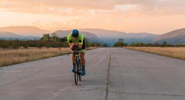 Triathlete riding his bicycle during sunset, preparing for a marathon. The warm colors of the sky provide a beautiful backdrop for his determined and focused effort. photo