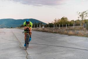 Triathlete riding his bicycle during sunset, preparing for a marathon. The warm colors of the sky provide a beautiful backdrop for his determined and focused effort. photo