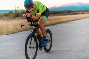 Triathlete riding his bicycle during sunset, preparing for a marathon. The warm colors of the sky provide a beautiful backdrop for his determined and focused effort. photo