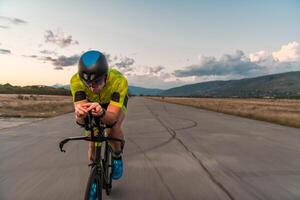 Triathlete riding his bicycle during sunset, preparing for a marathon. The warm colors of the sky provide a beautiful backdrop for his determined and focused effort. photo