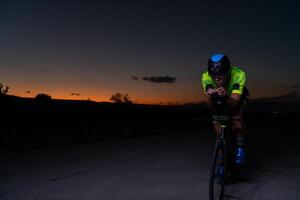 A triathlete rides his bike in the darkness of night, pushing himself to prepare for a marathon. The contrast between the darkness and the light of his bike creates a sense of drama and highlights the photo