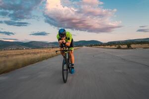 Triathlete riding his bicycle during sunset, preparing for a marathon. The warm colors of the sky provide a beautiful backdrop for his determined and focused effort. photo