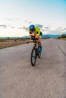 Triathlete riding his bicycle during sunset, preparing for a marathon. The warm colors of the sky provide a beautiful backdrop for his determined and focused effort. photo