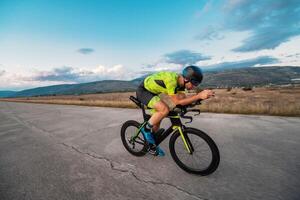 Triathlete riding his bicycle during sunset, preparing for a marathon. The warm colors of the sky provide a beautiful backdrop for his determined and focused effort. photo