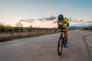 Triathlete riding his bicycle during sunset, preparing for a marathon. The warm colors of the sky provide a beautiful backdrop for his determined and focused effort. photo